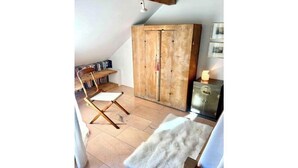 A cozy attic bedroom with a wooden wardrobe, a white chair, and a small table. - Great apartment in Ilanz (Ilanz Glion)