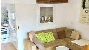 A living room with a beige sofa, a small round table, and a chair. There is a kitchen area visible to the left. - Great apartment in Ilanz (Ilanz Glion)