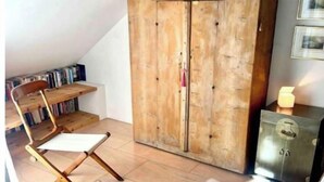 A cozy attic bedroom with a wooden wardrobe, a white chair, and a small table.