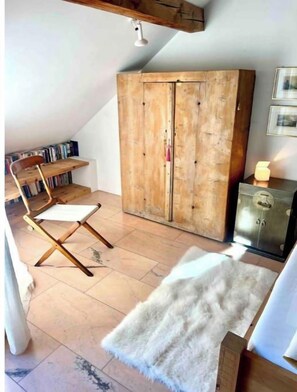 A cozy attic bedroom with a wooden wardrobe, a white chair, and a small table.