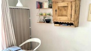 Un espace repas comprenant une table et des chaises en bois, un luminaire suspendu, un meuble en bois avec des étagères et un sol carrelé.