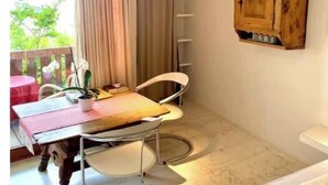 Une pièce de taille modeste comprenant un lit, une table à manger avec des chaises, un petit meuble en bois et une fenêtre avec des rideaux.