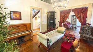 Una sala de estar con un piano de cola, un sofá y un sillón. Se ve una escalera que sube a otra habitación.