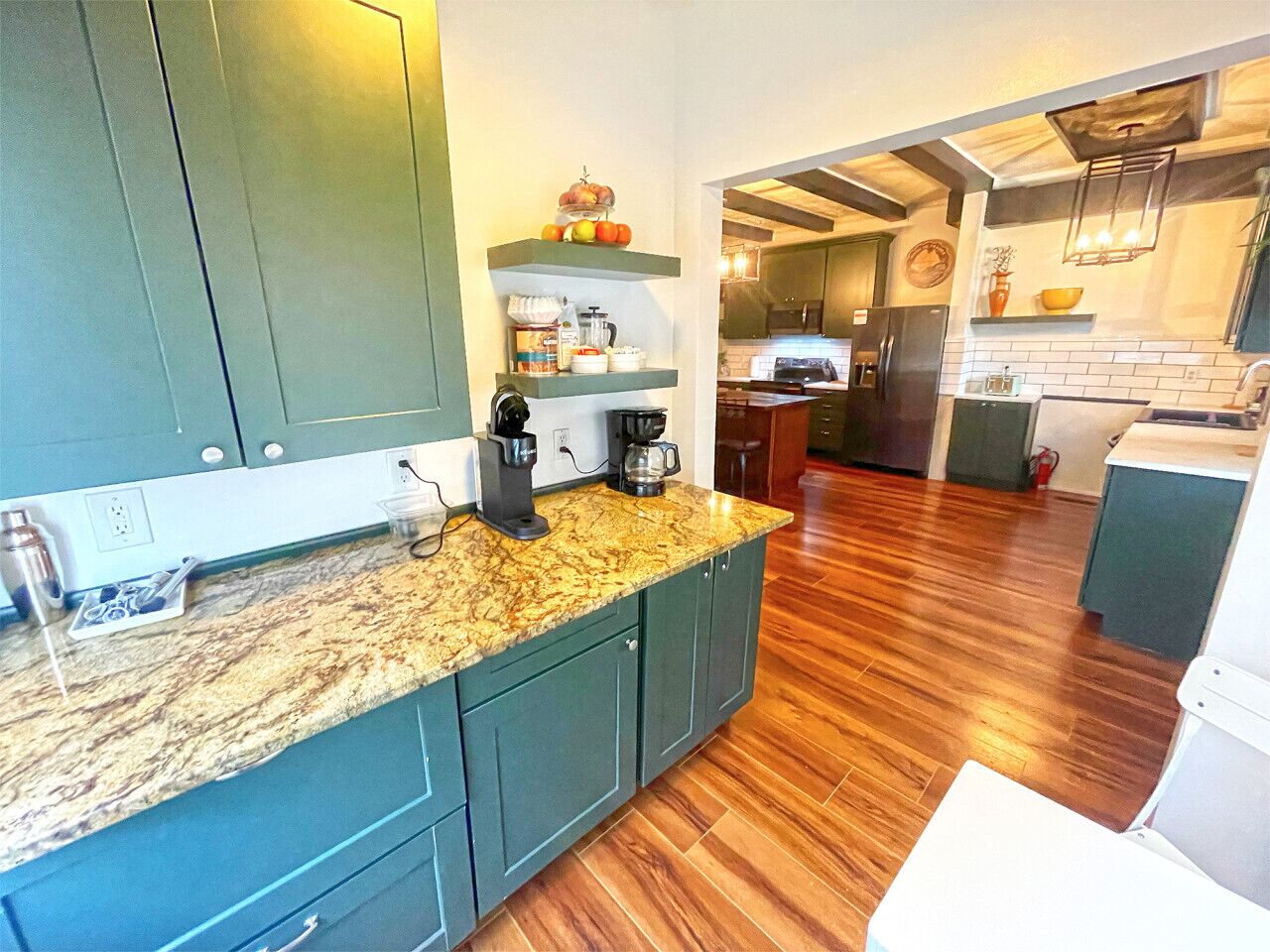 Une cuisine moderne avec des meubles de couleur verte, un plan de travail en granit et un revêtement de sol en bois.