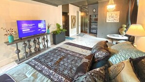 Una habitación de hotel moderna con una cama grande, televisión, una mesita y una lámpara decorativa.