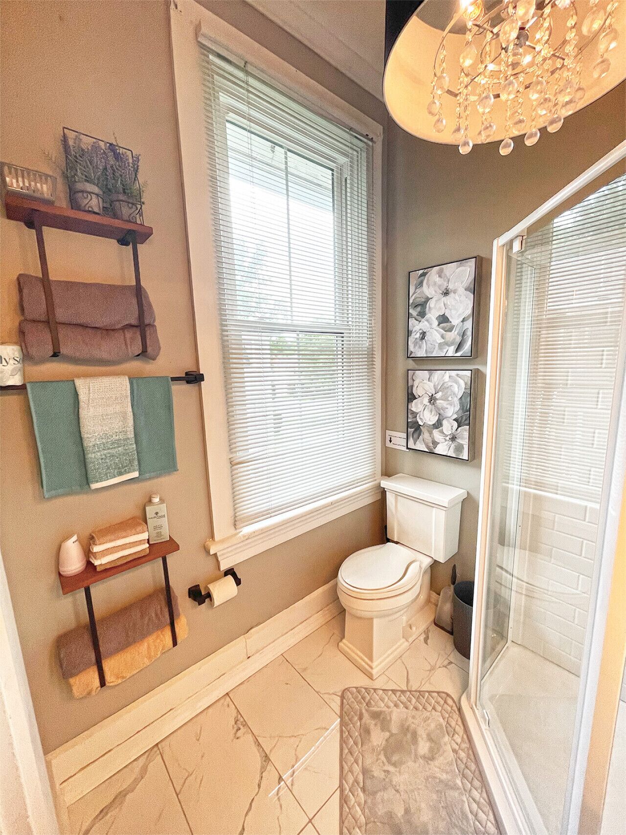 Une salle de bain comprenant des toilettes, une douche, un porte-serviettes et une fenêtre avec des stores.