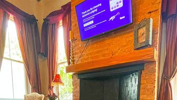 A room with a fireplace, a television screen, a table with a guidebook, and a window with curtains.