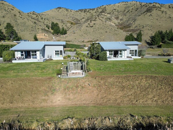 A modern two-story house with a large front lawn, a wooden deck, and a view of rolling hills in the background.