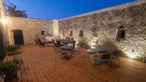 Un patio al aire libre con paredes de piedra, suelo de madera y mobiliario exterior.