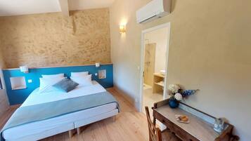 Habitación de hotel con cama, escritorio con espejo, mesita con un florero y un plato, y unidad de aire acondicionado.
