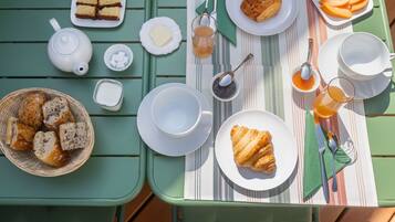 Una mesa dispuesta para el desayuno, con pan, bollería, mantequilla, mermelada, té y leche.