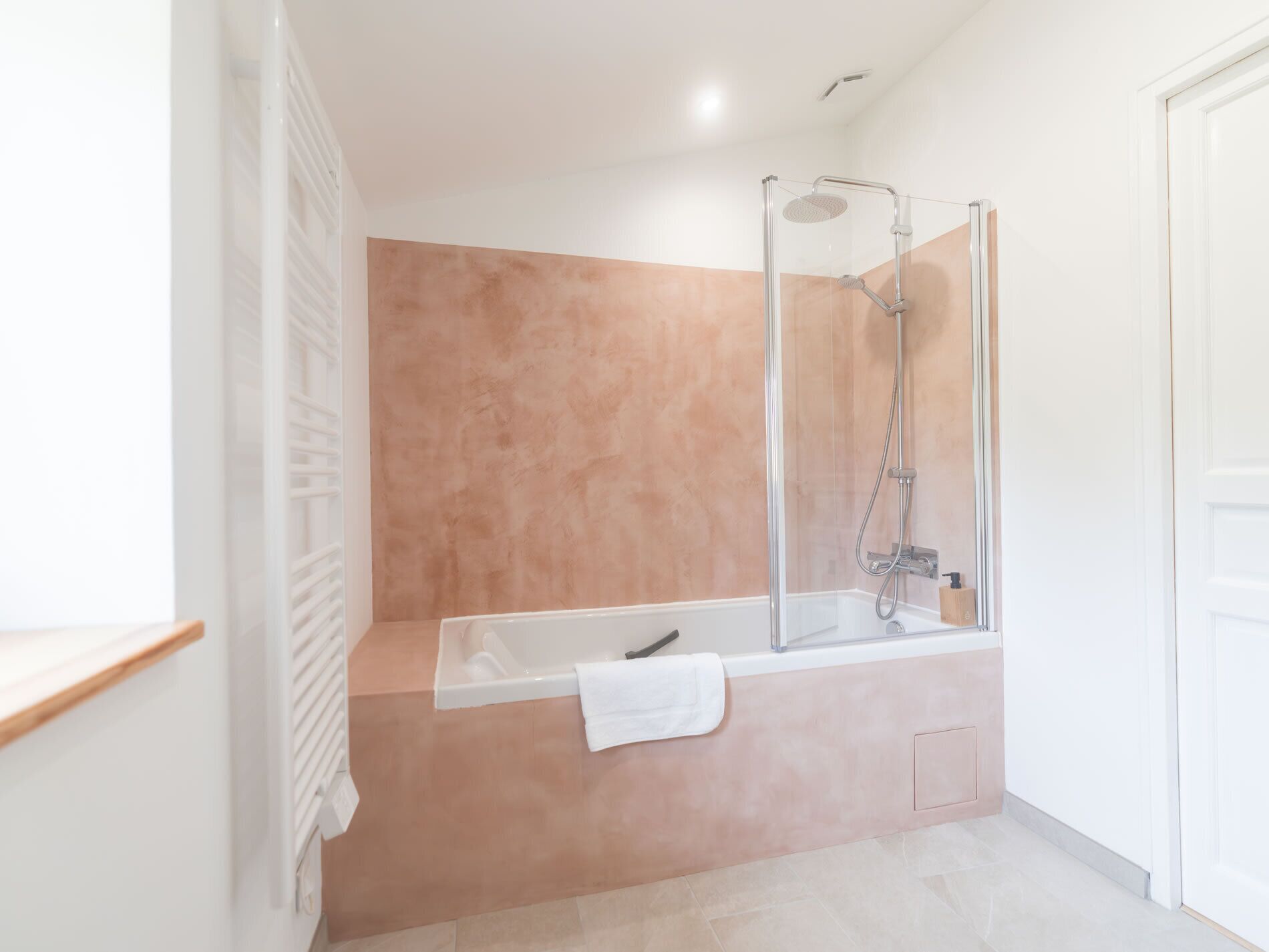 A modern bathroom with a glass-enclosed shower, a white bathtub, and a beige tiled wall.