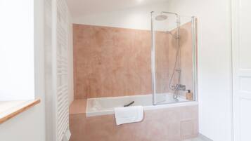 A modern bathroom with a glass-enclosed shower, a white bathtub, and a beige tiled wall.