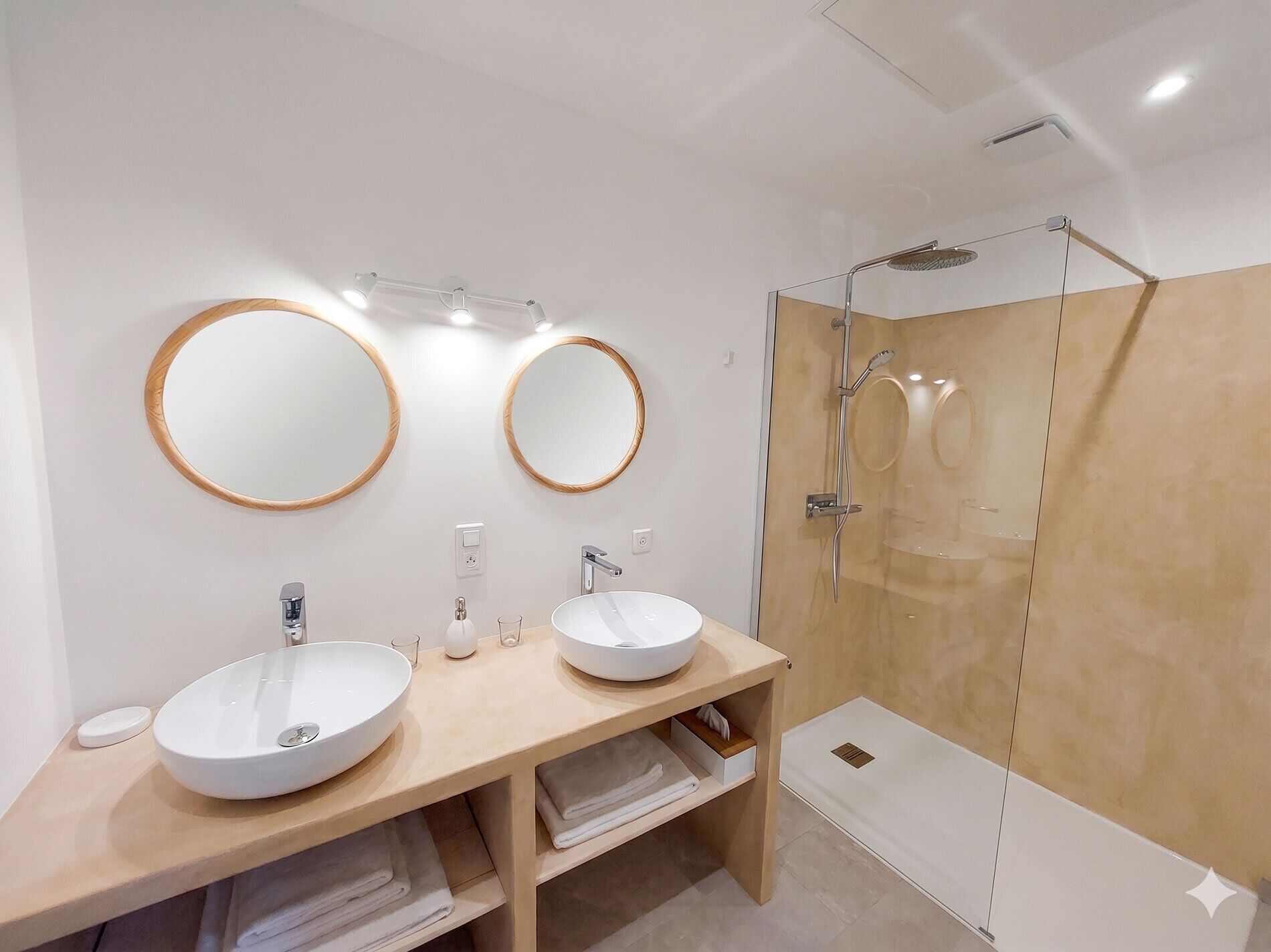 Un baño moderno con dos lavamanos, espejos, cabina de ducha de vidrio y un perchero para toallas.