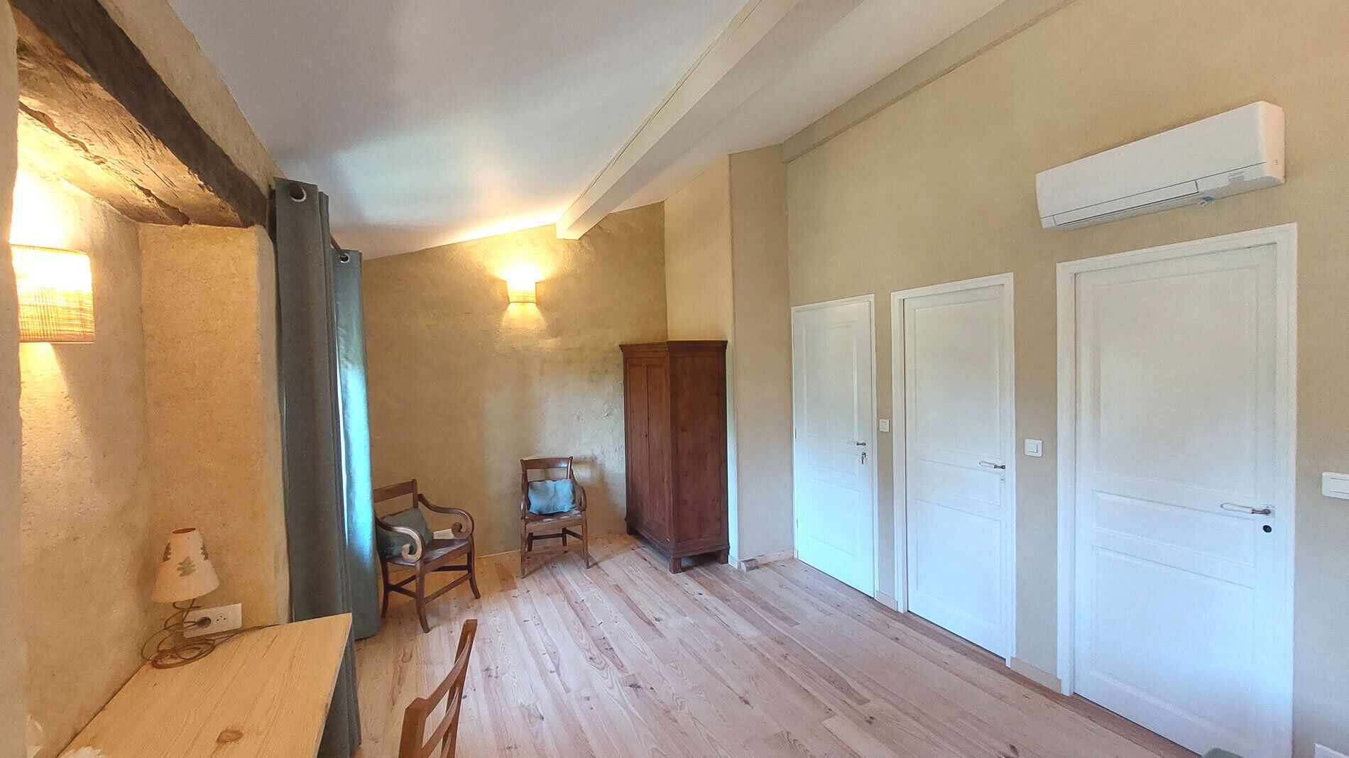 Habitación con piso de madera, un armario de madera, una silla y una mesa. Hay tres puertas blancas y un equipo de aire acondicionado en la pared.