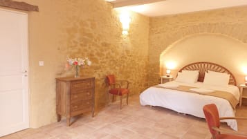 A bedroom with a stone wall, a wooden dresser, a bed with white bedding, and a red chair.