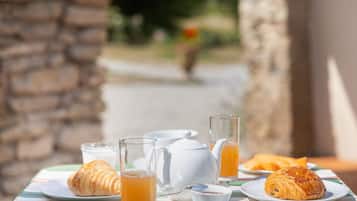 A breakfast setting with croissants, a teapot, and glasses of orange juice on a table.