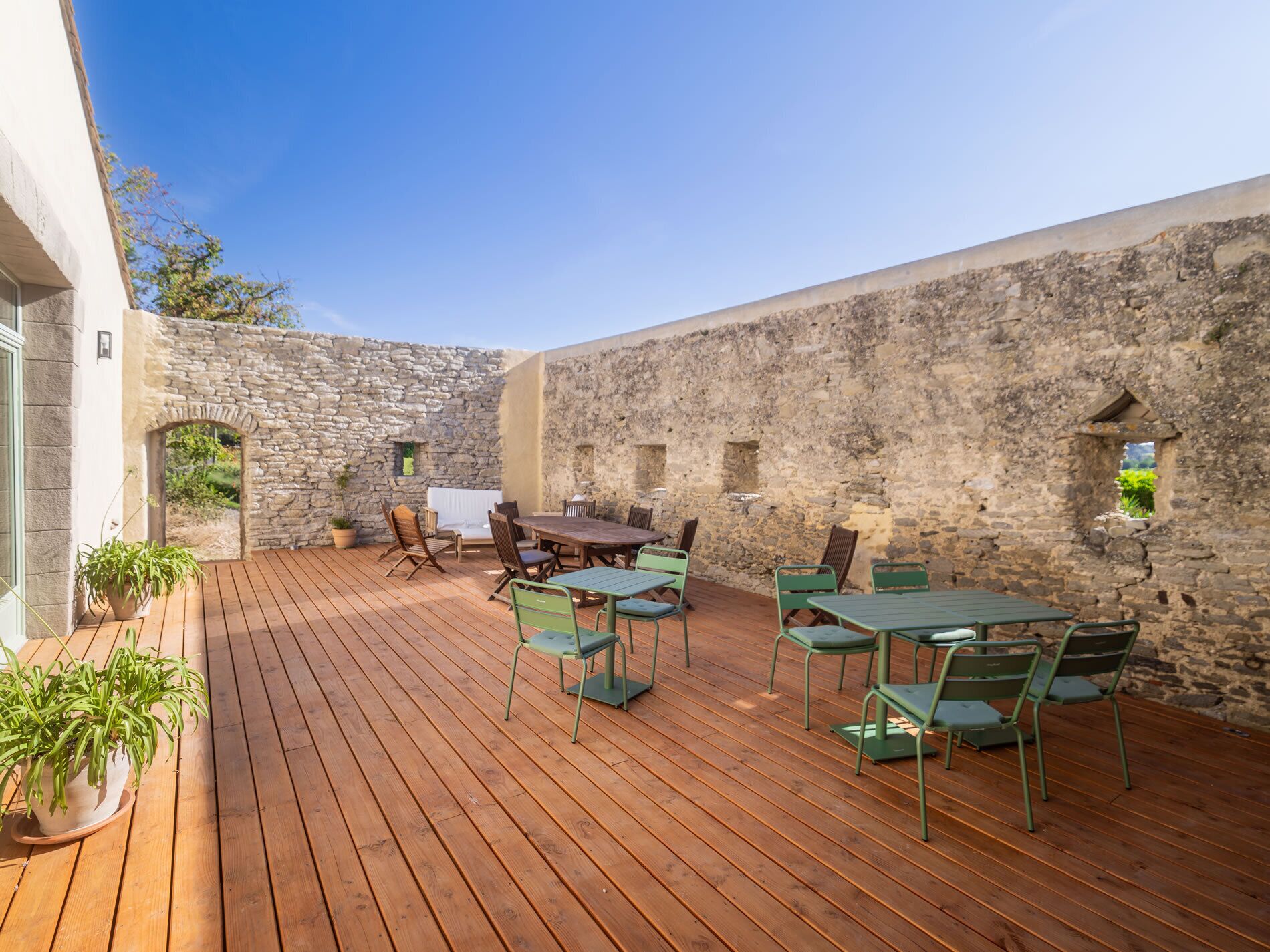 An outdoor patio with wooden flooring, stone walls, and green metal chairs and tables.