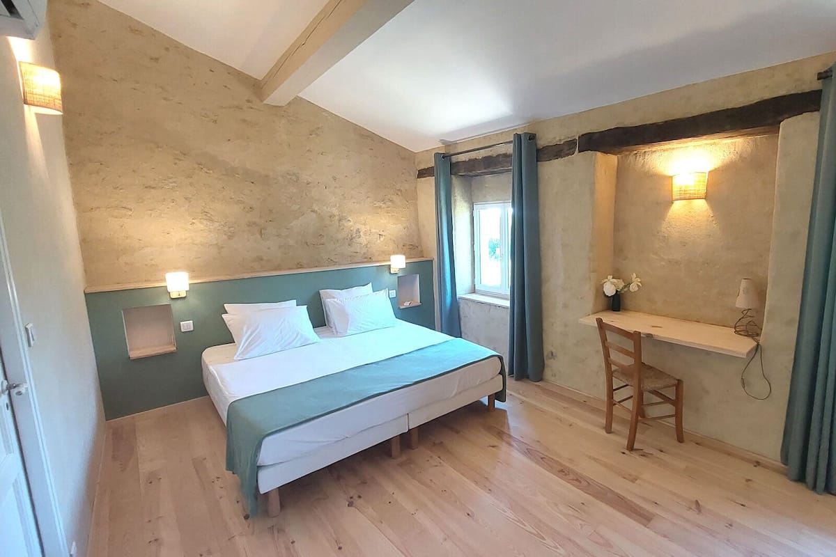 Un dormitorio con cama, escritorio, silla, ventana e iluminación en la pared.