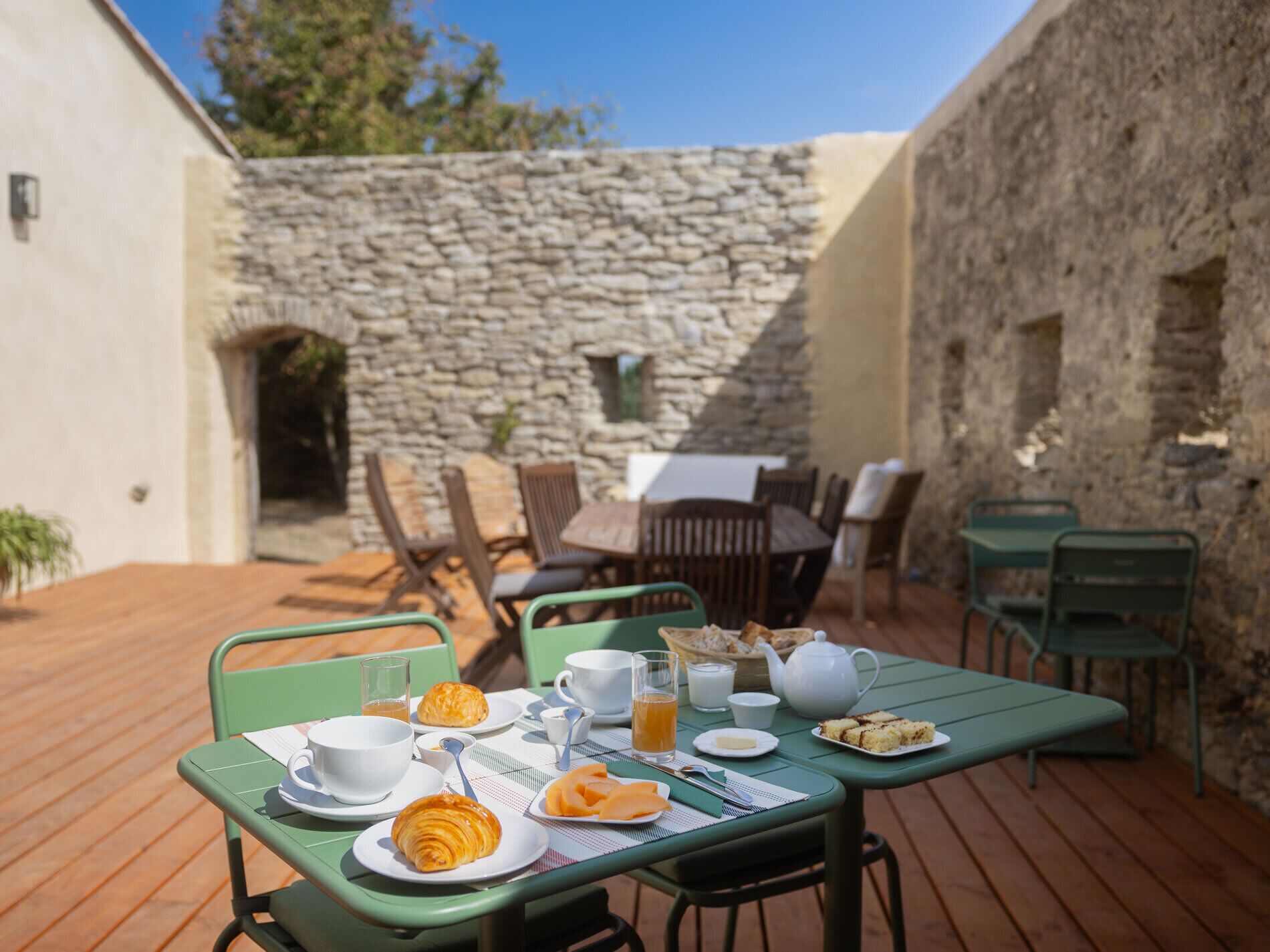 An outdoor dining area with a stone wall backdrop, wooden deck, and green metal furniture.