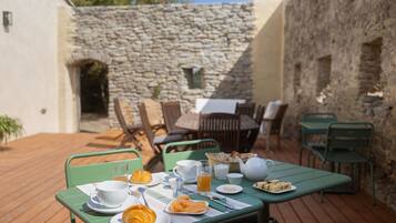 An outdoor dining area with a stone wall backdrop, wooden deck, and green metal furniture.