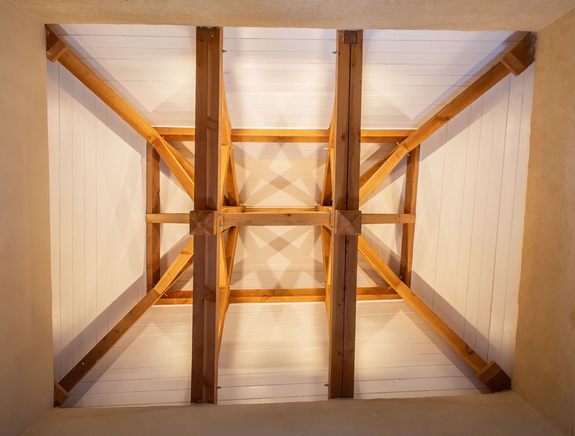 Quarto com estrutura de teto em madeira e paredes de painéis brancos.