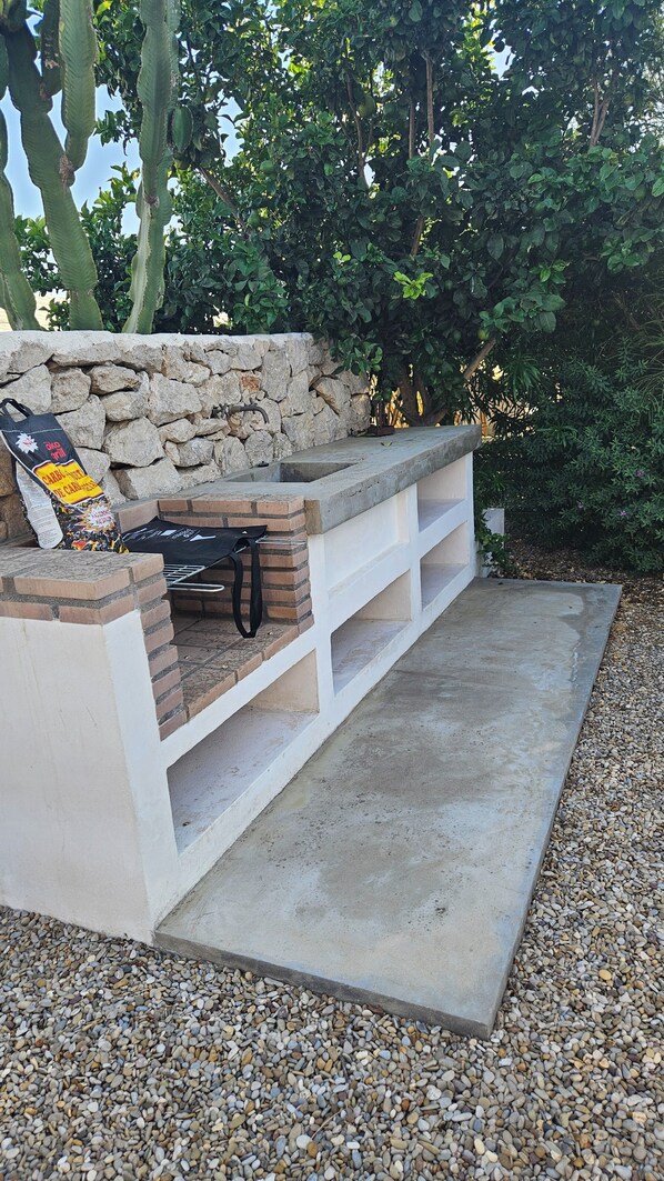 An outdoor barbecue area with a stone wall, a grill, and a seating bench.
