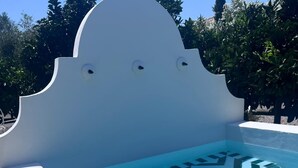 A swimming pool with a geometric tile pattern, a white wall, and a straw hat on the ground.