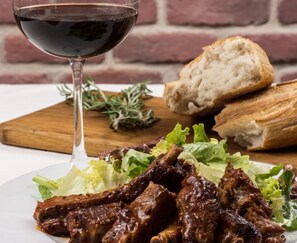 Una copa de vino tinto, un plato de carne y pan sobre una tabla de madera.