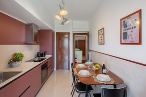 Una cocina moderna con comedor. Incluye estufa, fregadero y armarios. Se observa una mesa de comedor con platos, vasos y una botella.