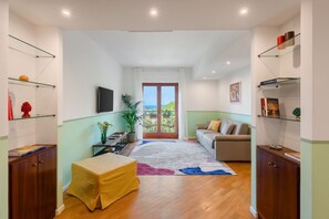 Una sala de estar moderna con un sofá, una mesa de centro y un televisor. Hay un balcón con vistas.