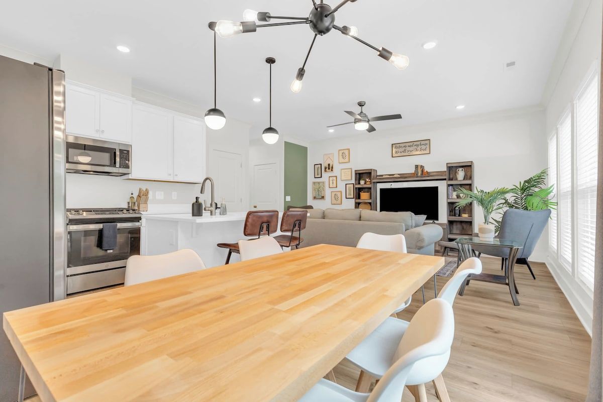Une cuisine moderne avec des meubles blancs, des appareils en acier inoxydable et une table à manger en bois.