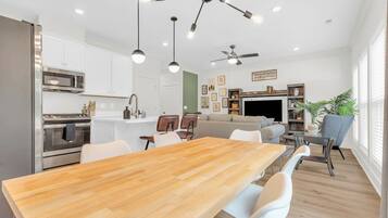 Une cuisine moderne avec des meubles blancs, des appareils en acier inoxydable et une table à manger en bois.