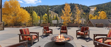 An outdoor seating area with fire pit, chairs, and a view of a mountainous landscape.