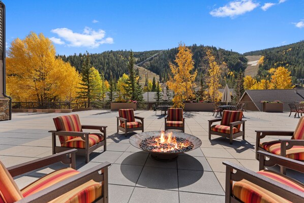 An outdoor seating area with fire pit, chairs, and a view of a mountainous landscape.