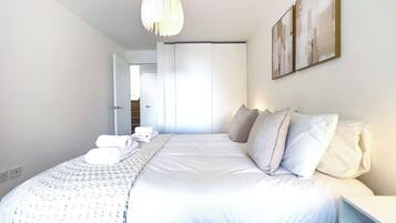 A modern bedroom with a large bed, white bedding, a hanging light fixture, and a painting on the wall.
