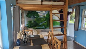 A cozy room with a bunk bed, a dining table with chairs, and a mural of a landscape on the wall. - Spend the night in a railroad carriage - nostalgia & comfort in Thuringia (Kirchheilingen)