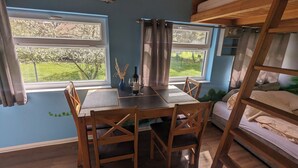 A room with a dining table, chairs, a bunk bed, and a window with a view of greenery. - Spend the night in a railroad carriage - nostalgia & comfort in Thuringia (Kirchheilingen)
