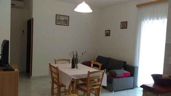 A dining area with a table and chairs, a sofa, and a television.