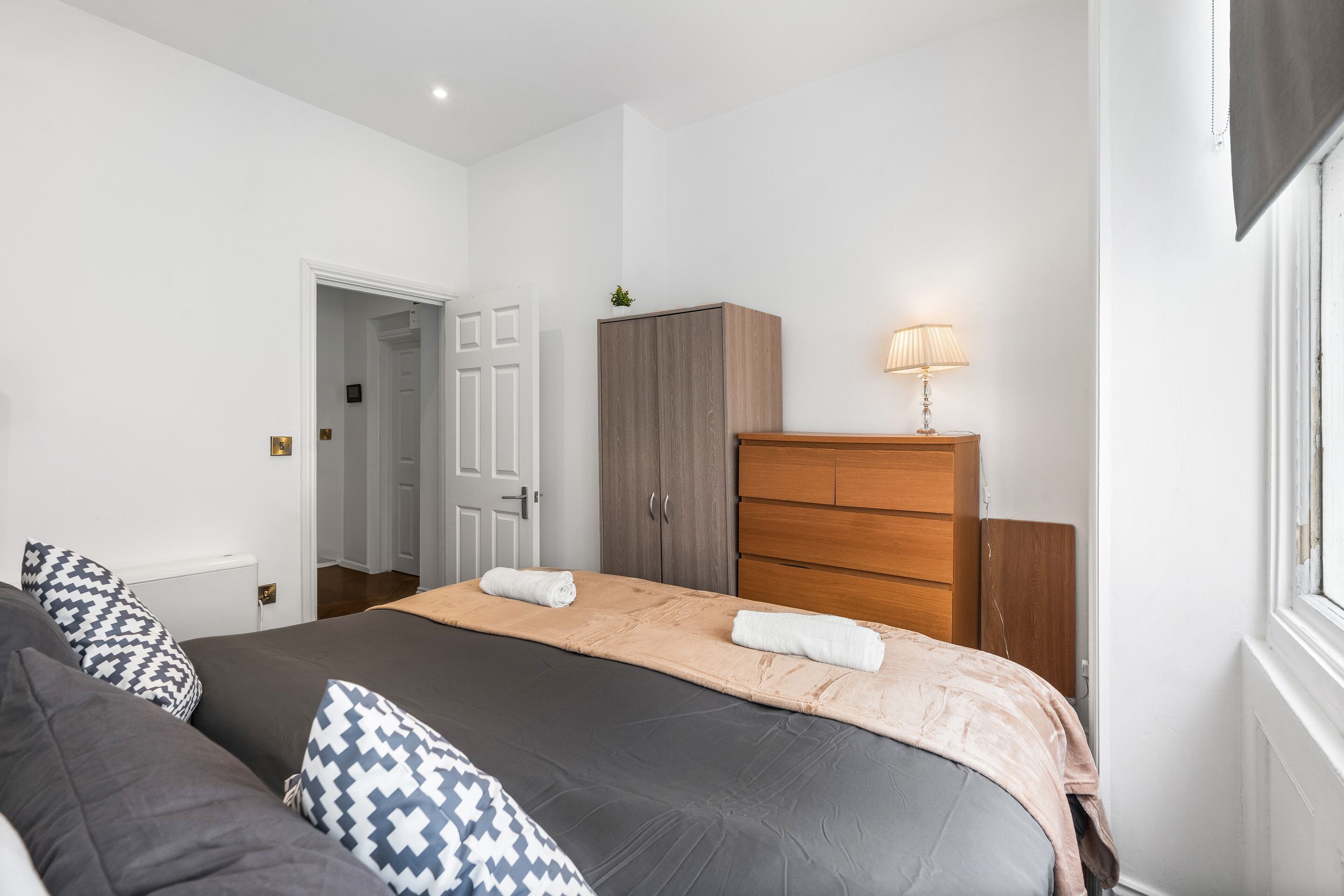 Une chambre à coucher comprenant un lit, une armoire en bois, une table de chevet avec une lampe et une porte donnant sur une autre pièce.
