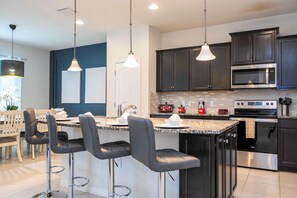 A modern kitchen with dark cabinets, stainless steel appliances, and a central island with bar stools.