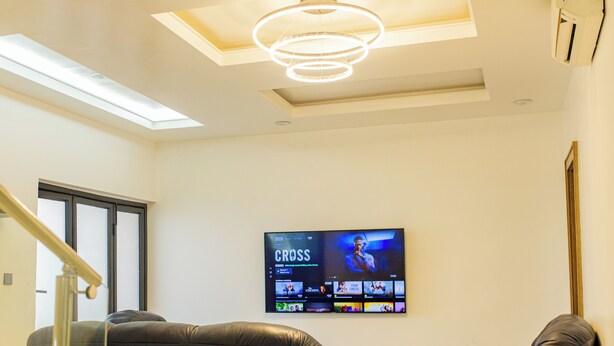 Ein modernes Wohnzimmer mit einem an der Wand montierten Flachbildfernseher, Ledersofas, einer Treppe mit Glastrennwand und einem Oberlicht.
