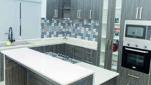 Eine moderne Küche mit grauen Schränken, einer zentralen Kochinsel, einer gemusterten Spritzschutzwand und integrierten Geräten, darunter eine Mikrowelle und ein Backofen.