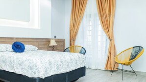 Ein Schlafzimmer mit einem Bett, zwei Stühlen, einer Lampe und Vorhängen.