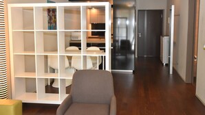 Een moderne woonkamer met een hoekbank, een witte tv-kast en een keuken met een koelkast en kasten.