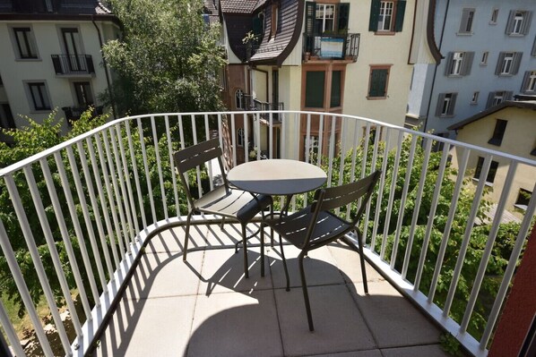 A balcony with a round table and two chairs, surrounded by a white metal railing.