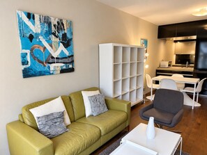 Een woonkamer met een groene bank, een witte salontafel, een grijze fauteuil en een witte boekenkast.
