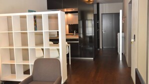 Een modern interieur met een witte schapunit, een grijze fauteuil en een keuken met donkere kastjes en een roestvrijstalen koelkast.