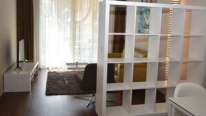 Een moderne kamer met een witte kastenwand, een bureau met een computer, een stoel en een groot raam met dunne gordijnen.
