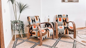 A room with two patterned armchairs, a small table with a bottle, a potted plant, and a framed artwork on the wall. - Riad Signature Medina  (Marrakech)